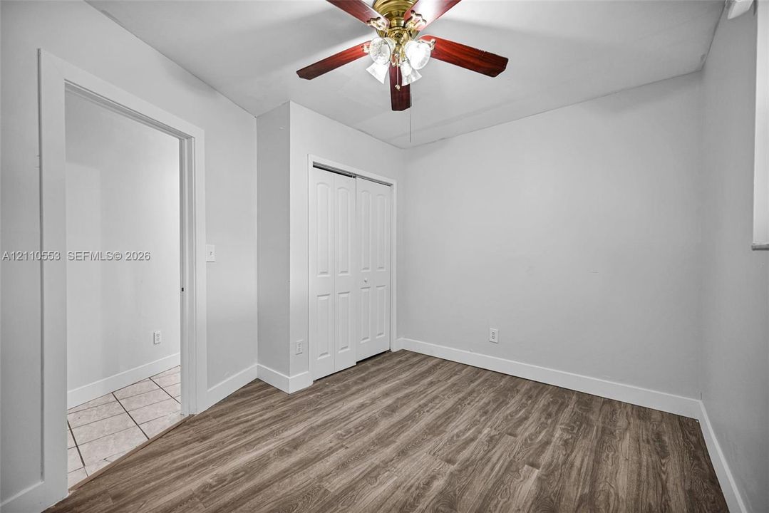 Room featuring wood-finish flooring, a ceiling fan with integrated lighting, and a dual-panel closet door