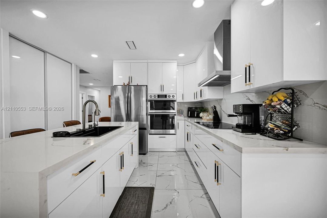 Modern kitchen featuring high-gloss white cabinetry, white stone-finish countertops, large-format veined tile flooring, built-in double wall ovens, and a center island with a matte black undermount sink