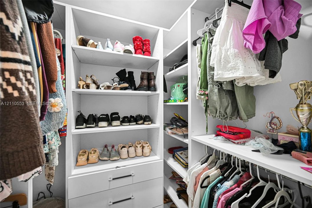 Custom white cabinetry featuring integrated shelving, pull-out drawers with bar-style pulls, and tiered garment hanging rods