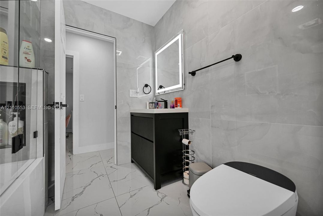 Bathroom featuring large-format porcelain tile wall cladding, a black floating vanity with a solid surface countertop, an LED-backlit mirror, and matte black hardware