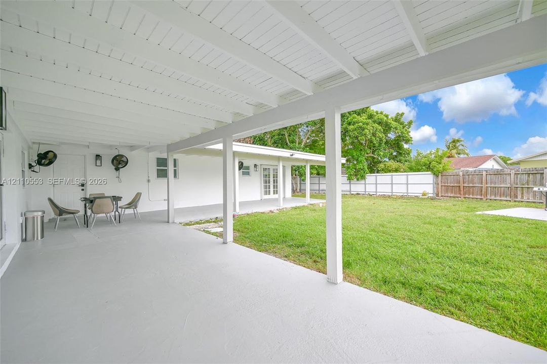 Covered patio featuring white beamed ceilings, painted concrete flooring, and an expansive lawn enclosed by wood-panel fencing