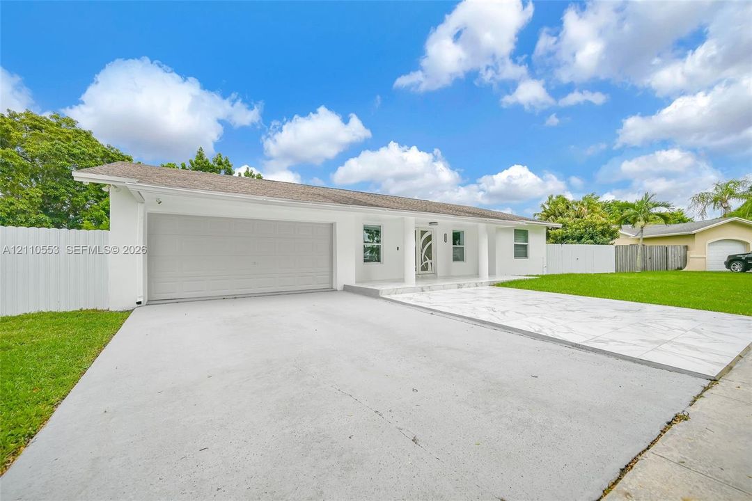 Single-story exterior featuring white stucco siding, a tiled front patio, attached two-car garage, and perimeter privacy fencing