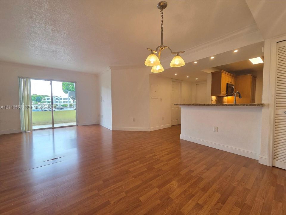 Open-concept area featuring wood-finish flooring, a breakfast bar with stone-surface countertop, three-arm pendant lighting, and a glass sliding door