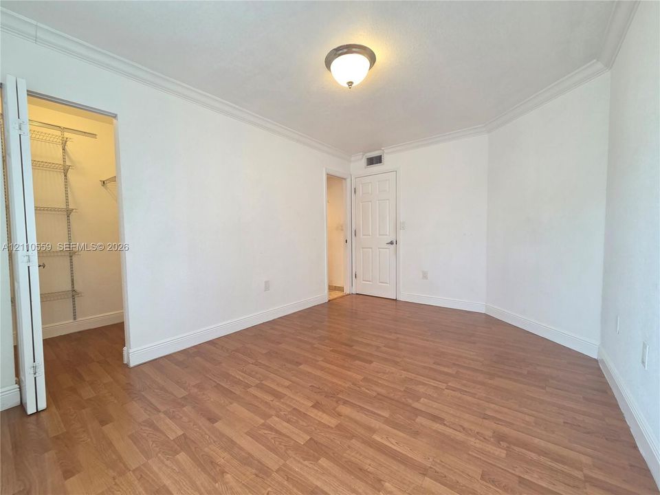Room featuring wood-finish flooring, crown molding, a built-in wire shelving system within the closet, and a ceiling-mounted light fixture