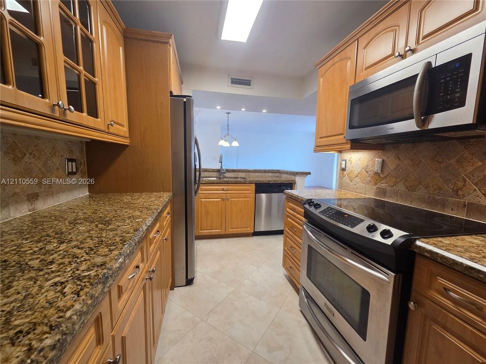 Kitchen featuring natural wood cabinetry, stone countertops, a tiled backsplash, stainless steel appliances, and tile flooring
