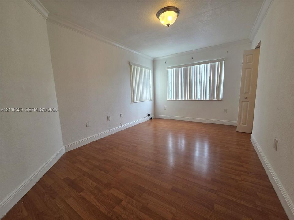 Interior room featuring wood-finish flooring, crown molding, dual windows with vertical blinds, and a semi-flush mount ceiling fixture