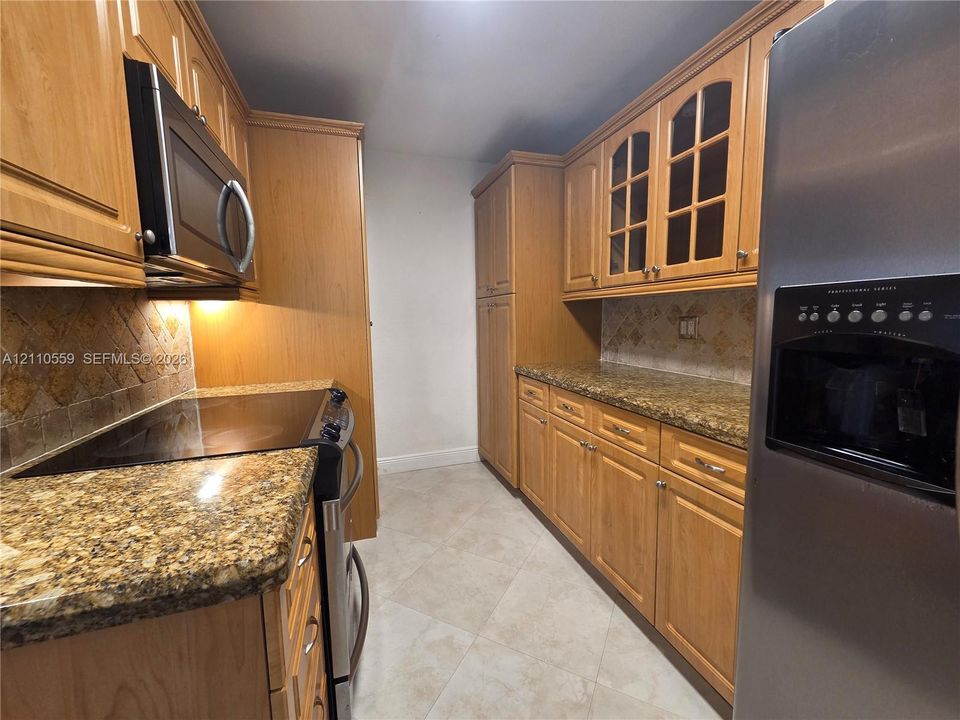 Kitchen featuring natural wood cabinetry, stone countertops, glass-panel upper cabinet doors, tile backsplash, and stainless steel appliances