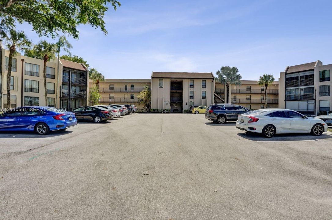 Multi-story building exterior featuring paved surface parking and mature palm trees