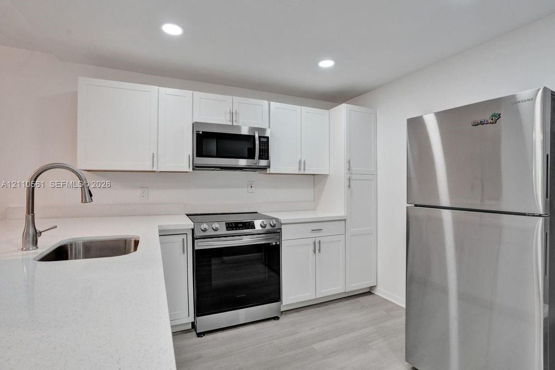 Kitchen featuring white shaker-style cabinetry, solid-surface countertops, recessed lighting, wood-finish flooring, and stainless steel appliances