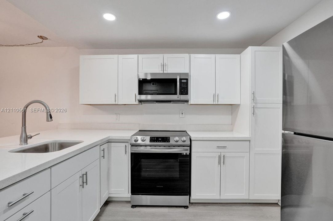 Kitchen featuring white shaker-style cabinetry, quartz countertops, stainless steel appliances, a pull-down kitchen faucet, and recessed lighting