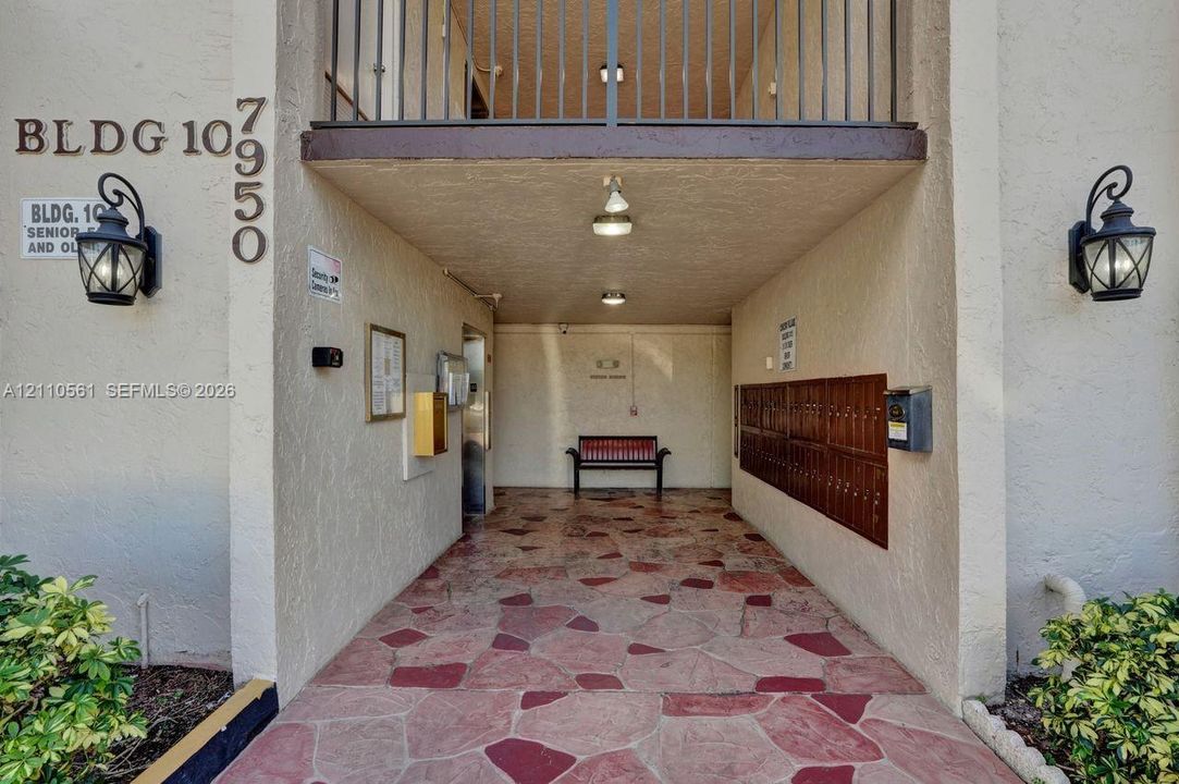 Covered building entrance featuring flagstone-style paving, wall-mounted carriage-style light fixtures, and integrated mailboxes