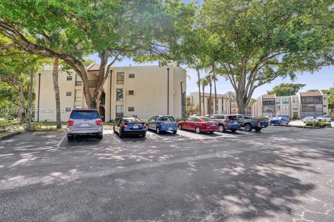 Multi-story stucco exterior buildings featuring paved surface parking and mature canopy trees