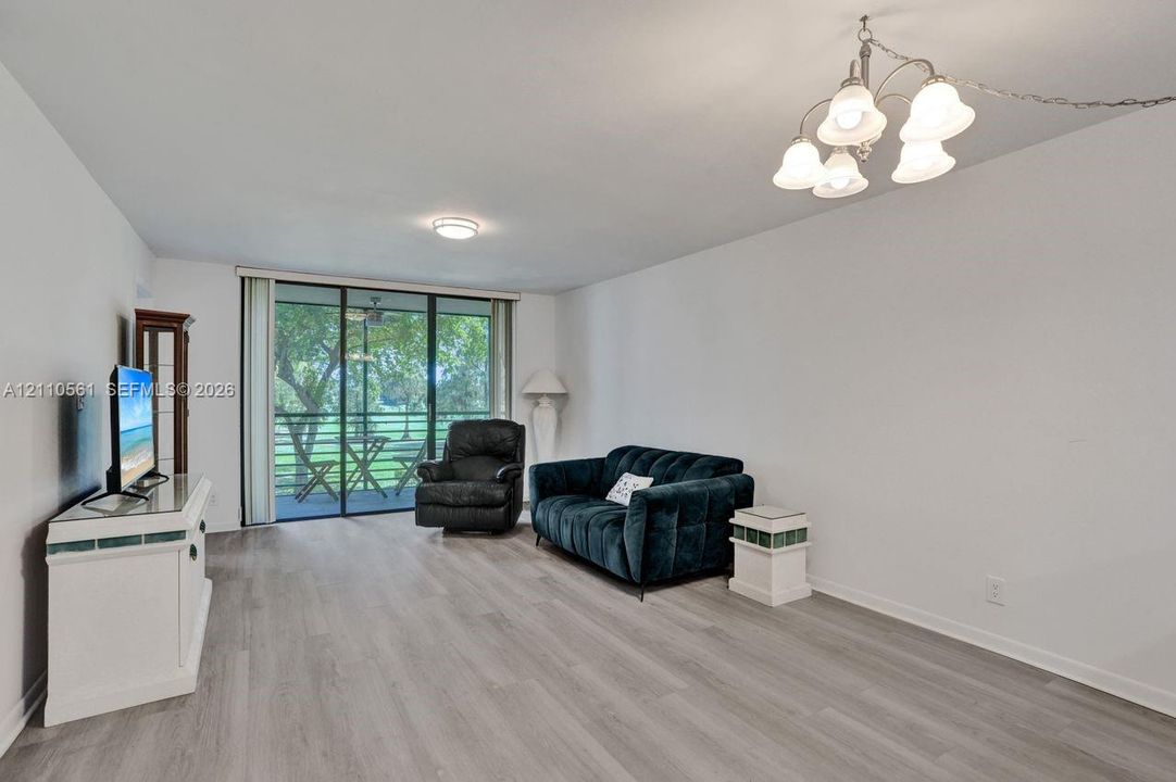 Living area featuring wood-finish flooring, a multi-light chandelier, a ceiling-mounted light fixture, and sliding glass doors with screen enclosure