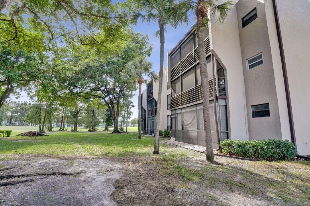 Multi-story residential building exterior featuring stucco siding, multi-level screened-in balconies, and mature landscaping