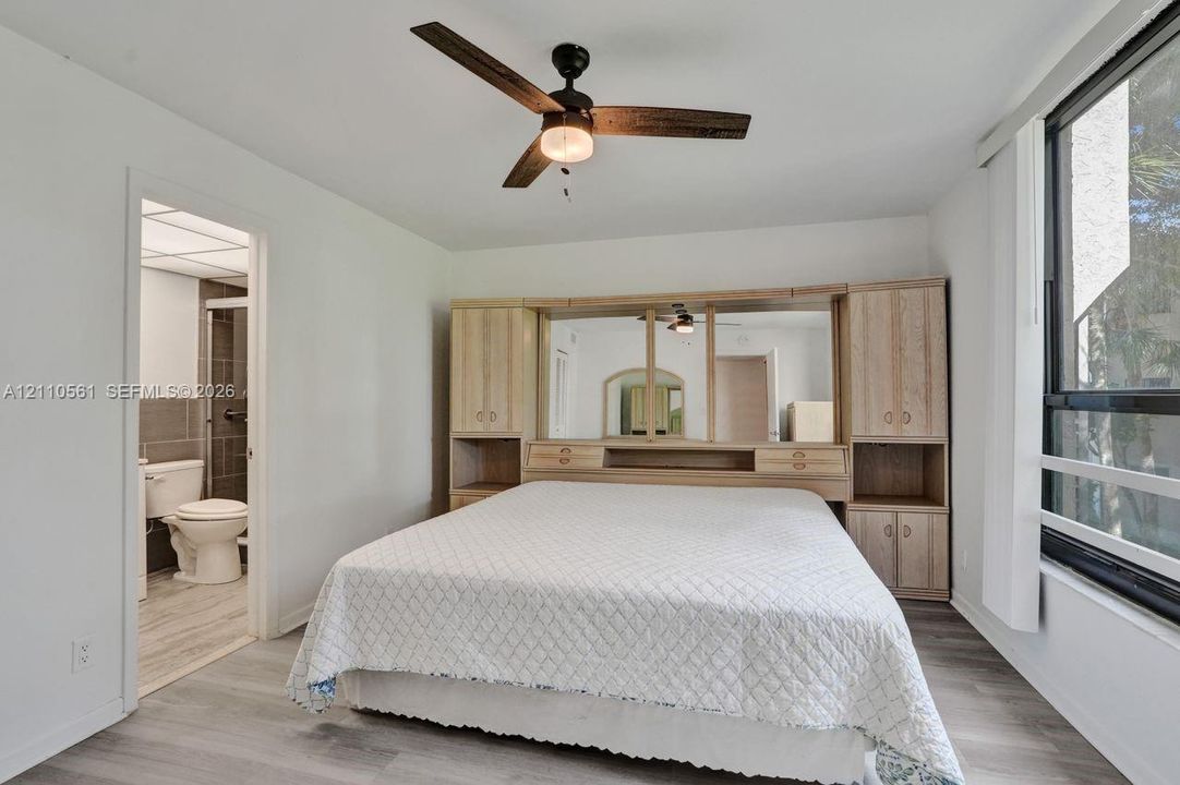 Room featuring light wood-finish flooring, a ceiling fan with integrated lighting, a large window, and built-in wood cabinetry with central mirrored panels