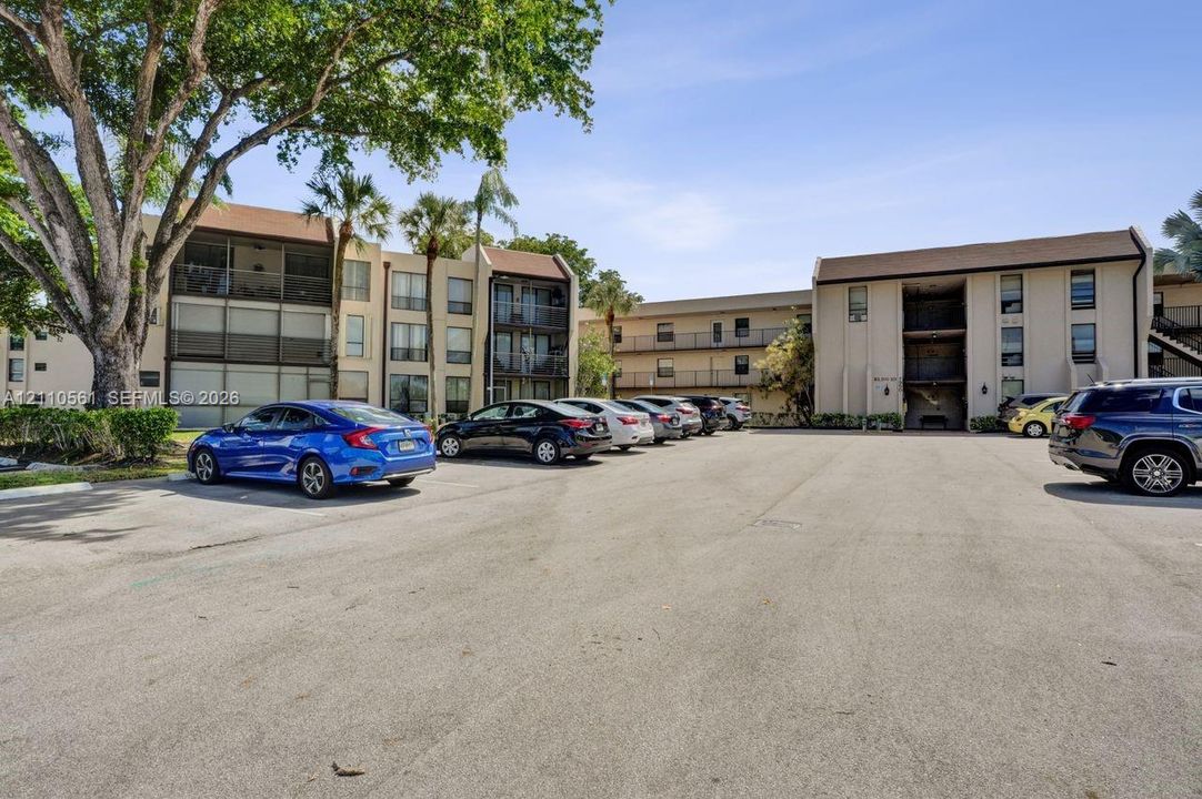 Multi-story complex exterior featuring neutral stucco siding, pitched roofs, screen-enclosed balconies, and mature landscaping