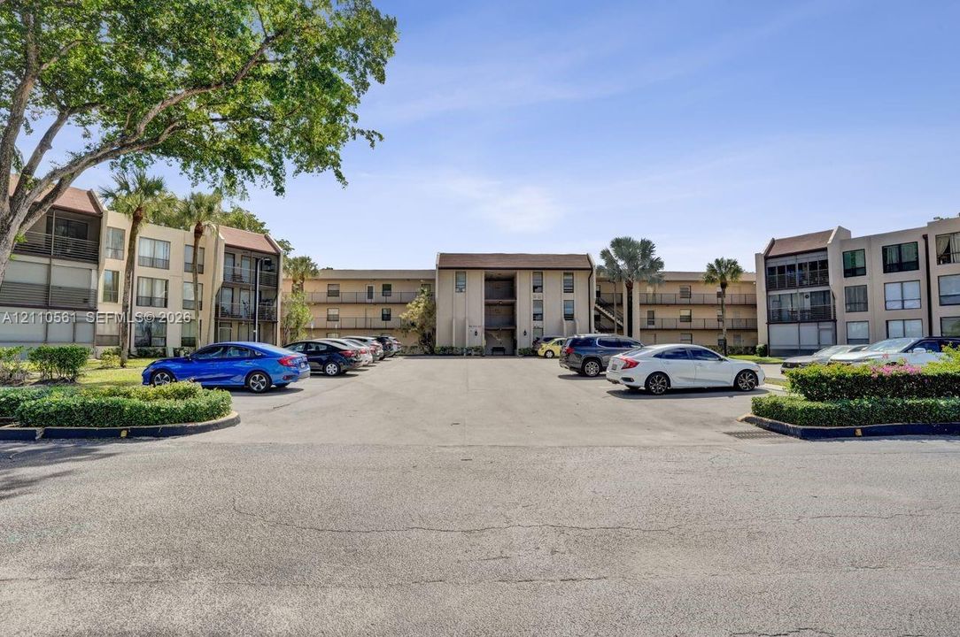 Multi-story exterior featuring a neutral stucco facade, shingled roofing, integrated balconies, and mature landscaping