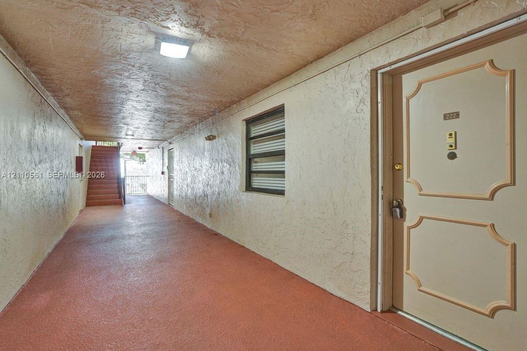 Covered exterior walkway with textured ceiling, flush-mount lighting, and solid-core paneled entry door