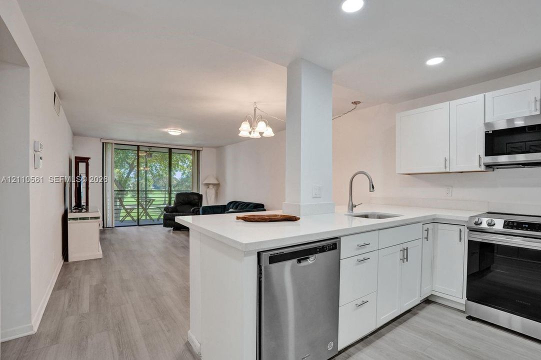 Kitchen featuring white cabinetry, solid surface countertops, stainless steel appliances, and wood-finish flooring