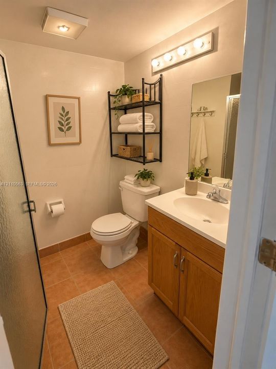 Bathroom featuring wood-finish vanity cabinetry with an integrated sink, tiled flooring, wall-mounted light fixture, and walk-in shower with a glass door