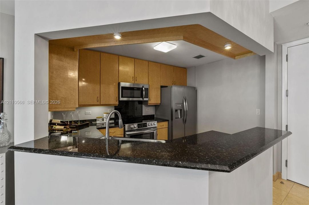 Kitchen featuring wood cabinetry, stone countertops, stainless steel appliances, a breakfast bar, and integrated recessed lighting