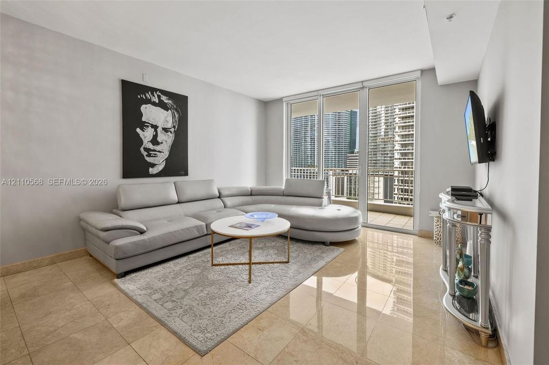 Living area featuring neutral-toned tile flooring, floor-to-ceiling glass panel doors, and an attached balcony