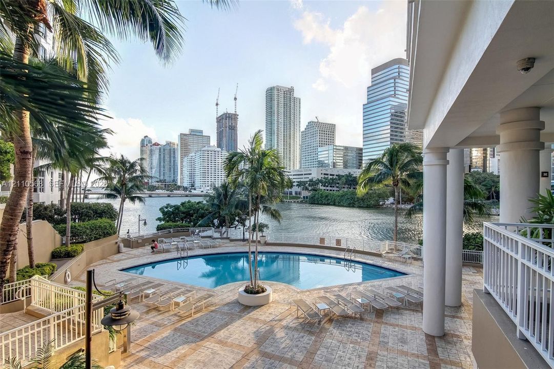 Covered terrace with structural columns, stone-paved pool deck, swimming pool, and water frontage