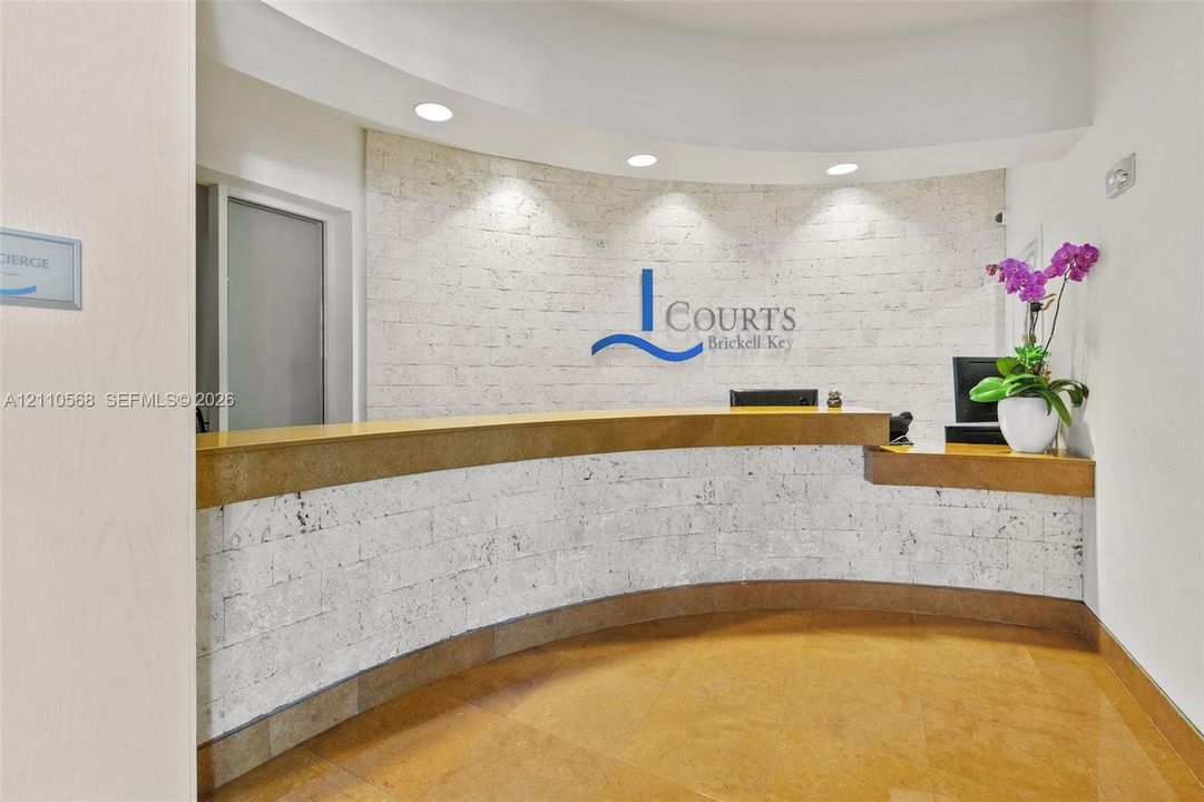 Concierge reception desk featuring a curved stone-clad counter, textured stone wall paneling, and integrated recessed lighting