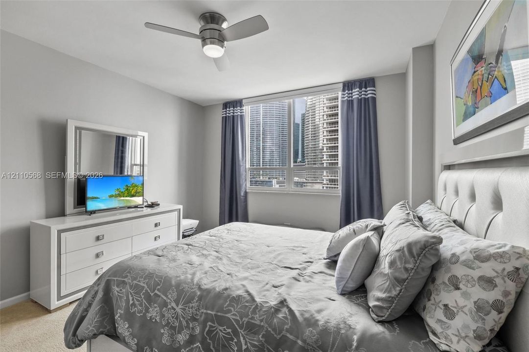 Neutral-toned interior featuring a ceiling fan with integrated lighting and a large window with urban exterior exposure