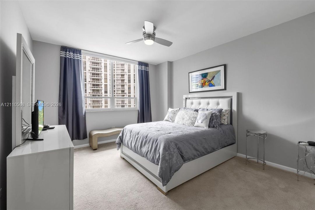 Neutral-toned bedroom featuring wall-to-wall carpeting, large windows, and a ceiling-mounted light fixture with fan