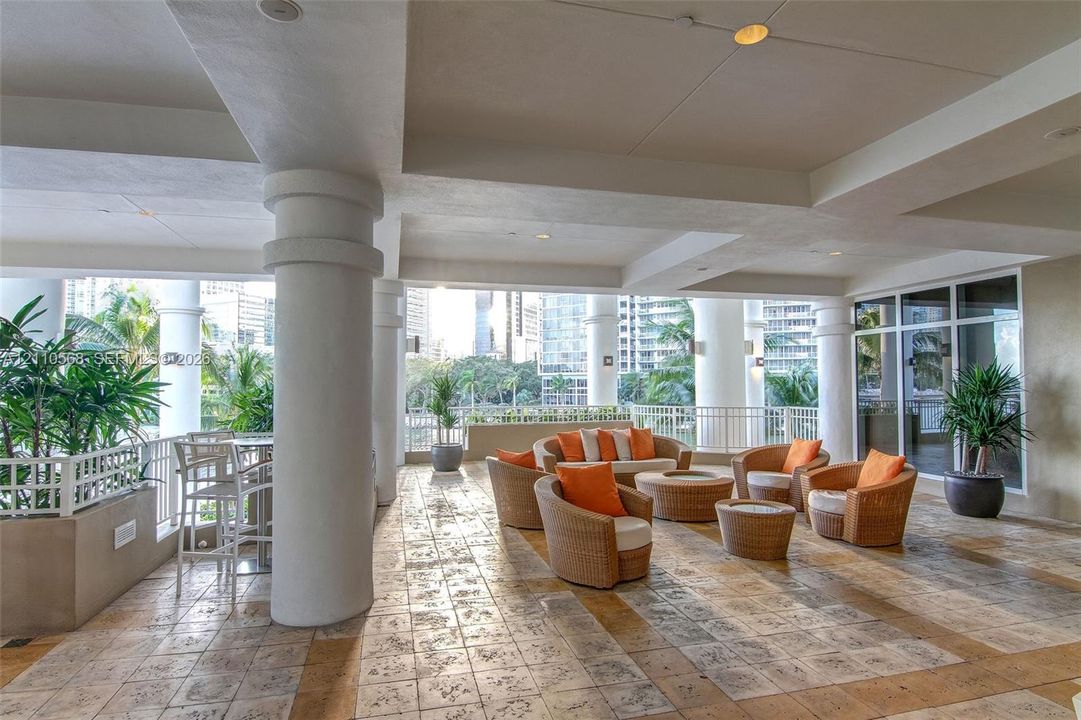 Covered outdoor terrace featuring stone tile flooring, prominent architectural columns, recessed ceiling lighting, and metal perimeter railing