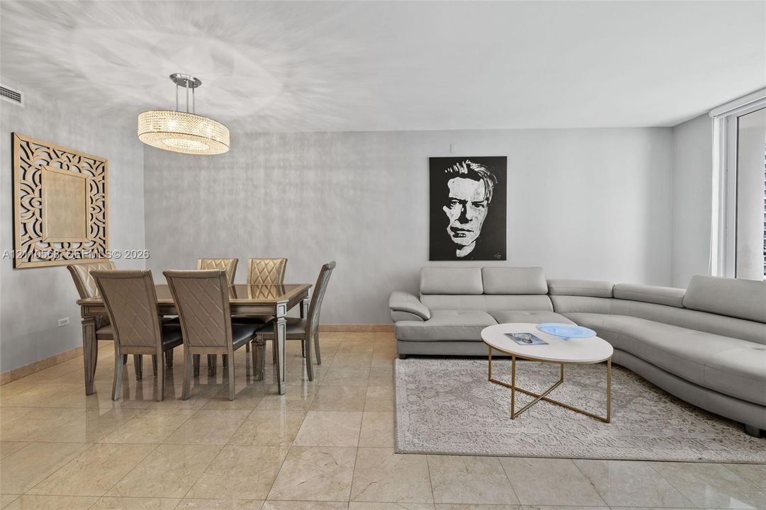 Open-concept living space featuring large-format tile flooring, textured wall finishes, and a contemporary drum-style chandelier with a crystalline fringe