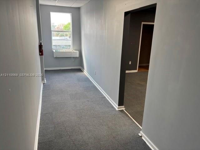Neutral-toned workspace featuring wall-to-wall carpeting, an integrated window HVAC unit, and a rectangular window providing natural light