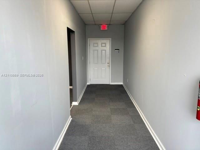 Interior hall featuring a six-panel door, neutral gray wall finish, and modular carpet tile flooring