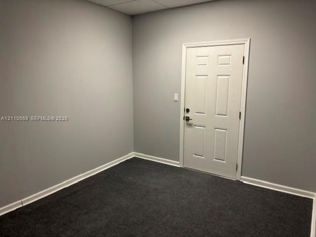 Neutral interior featuring gray walls, dark charcoal carpeting, and a six-panel door with metallic hardware