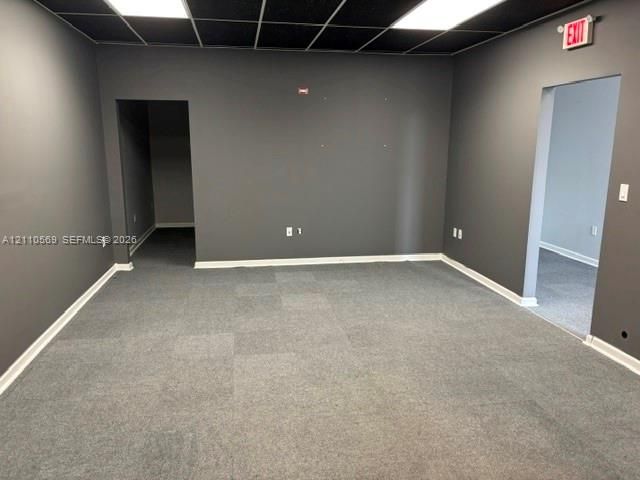 Interior room featuring grey carpeting, charcoal wall finishes, a drop ceiling with recessed panel lighting, and two entryway openings