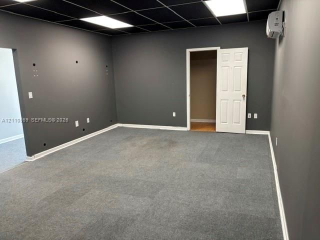 Interior room featuring wall-to-wall carpeting, a black drop ceiling with recessed panel lighting, and a wall-mounted ductless HVAC unit