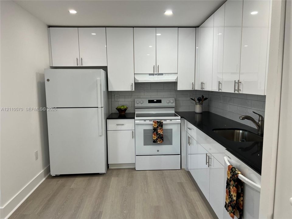 Kitchen featuring high-gloss white cabinetry, contrasting dark countertops, gray subway tile backsplash, stainless steel sink with arch faucet, and wood-finish flooring