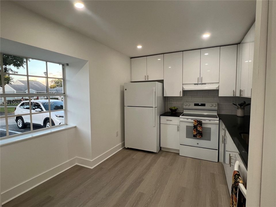 Kitchen featuring white high-gloss cabinetry, black countertops, wood-finish flooring, recessed lighting, and a multi-pane window