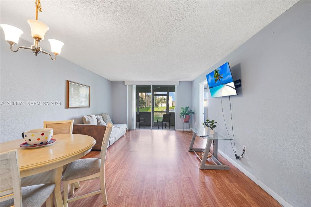 Open-concept area featuring wood-finish flooring, a traditional multi-arm chandelier, and sliding glass doors with access to an exterior balcony