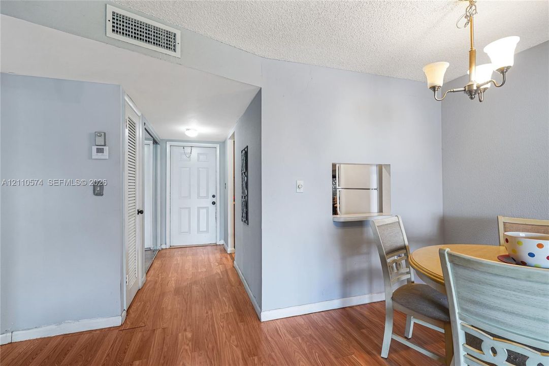Interior space featuring wood-finish flooring, a pass-through wall opening, a multi-arm chandelier, and a paneled entry door