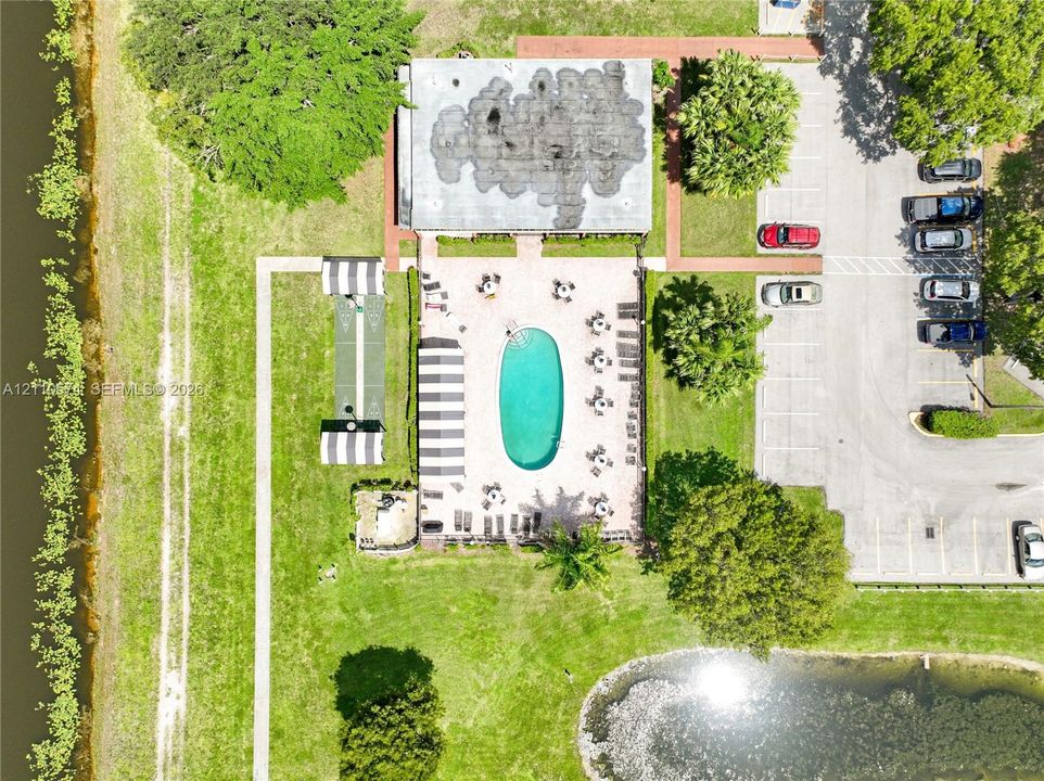 Aerial perspective of the property grounds featuring an oval swimming pool, paved pool deck, bocce ball court, and on-site parking area