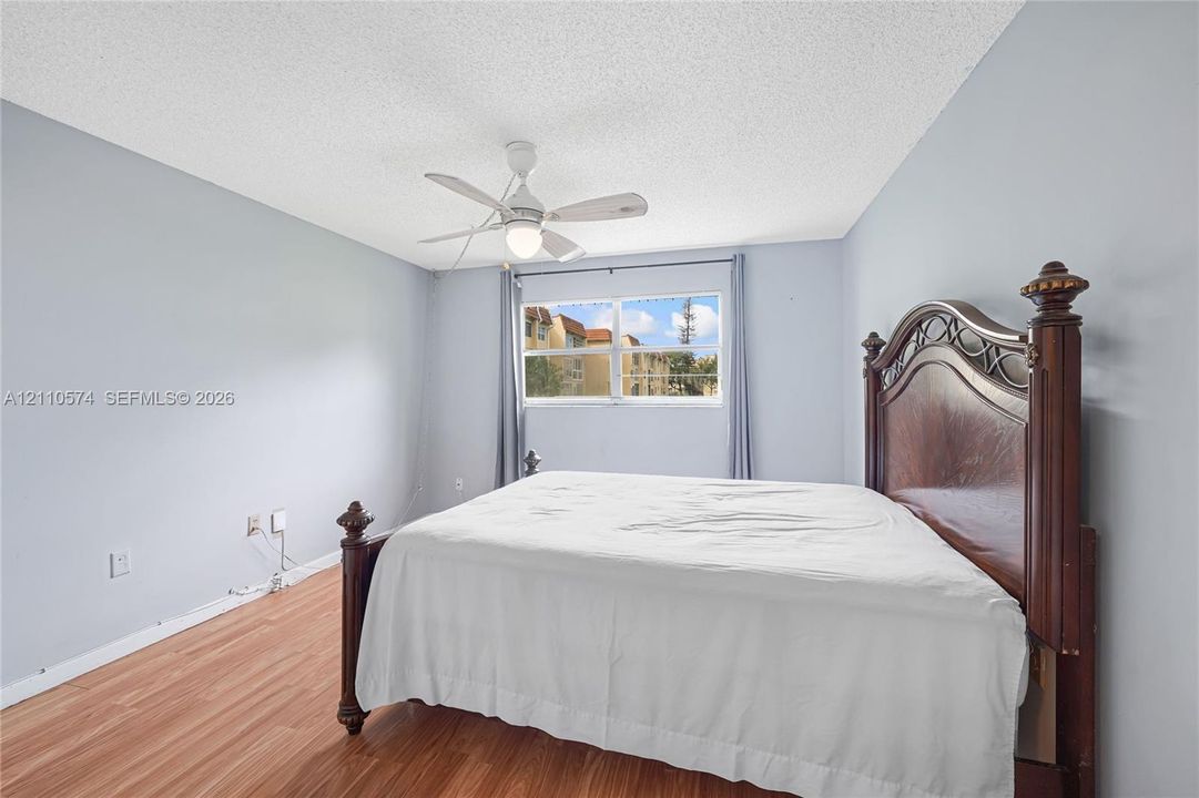 Bedroom featuring wood-finish flooring, a white ceiling fan with integrated lighting, and a single-pane window