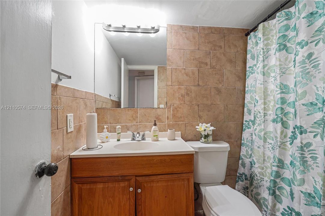 Second bathroom featuring a wood-finish vanity with a white countertop and integrated sink, earth-toned wall tile, wall-mounted light fixture, and a white toilet