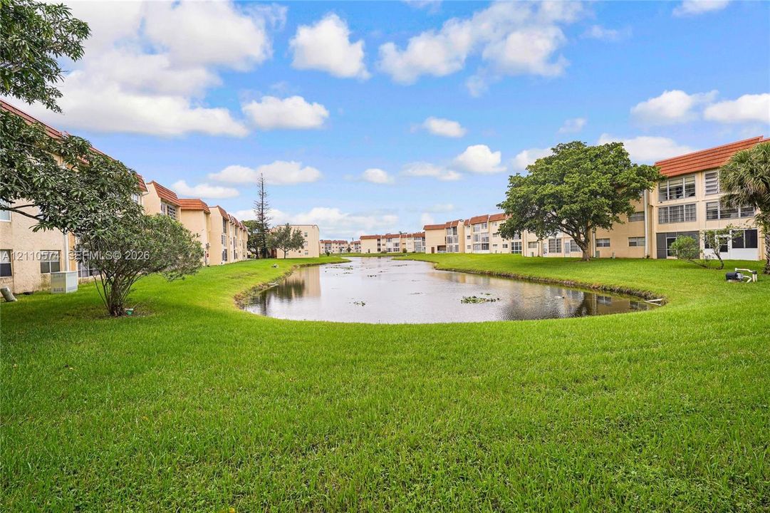 Multi-story stucco exterior buildings featuring a central pond, mature trees, and expansive lawn space