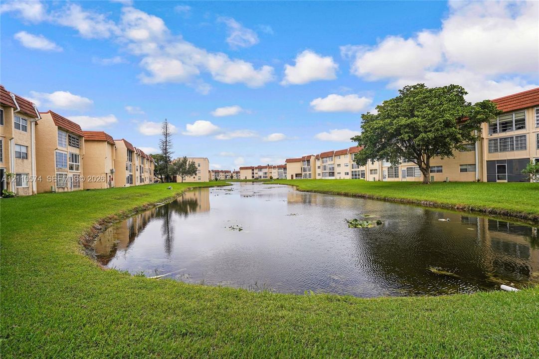 Waterfront residential complex featuring multi-story masonry construction, red tile roofing, and expansive green space surrounding a central retention pond