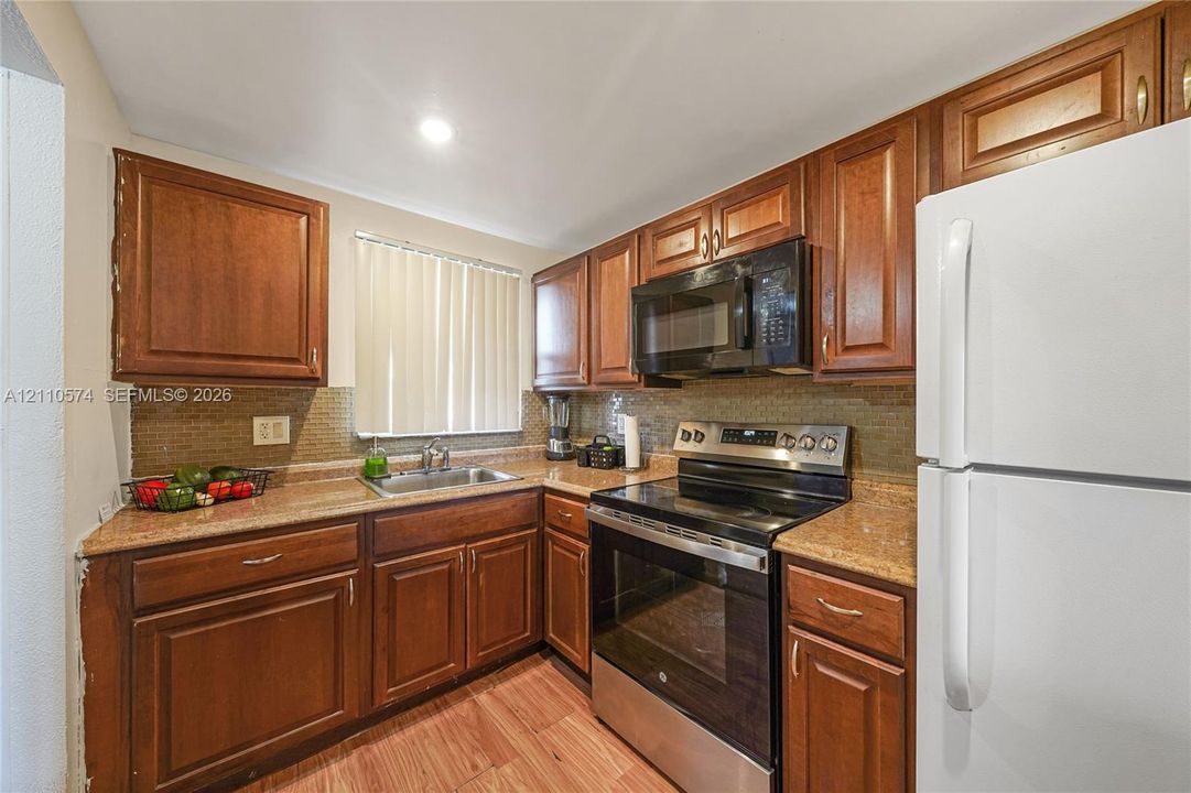 Kitchen featuring wood cabinetry, stone-surface countertops, mosaic tile backsplash, stainless steel appliances, and wood-finish flooring