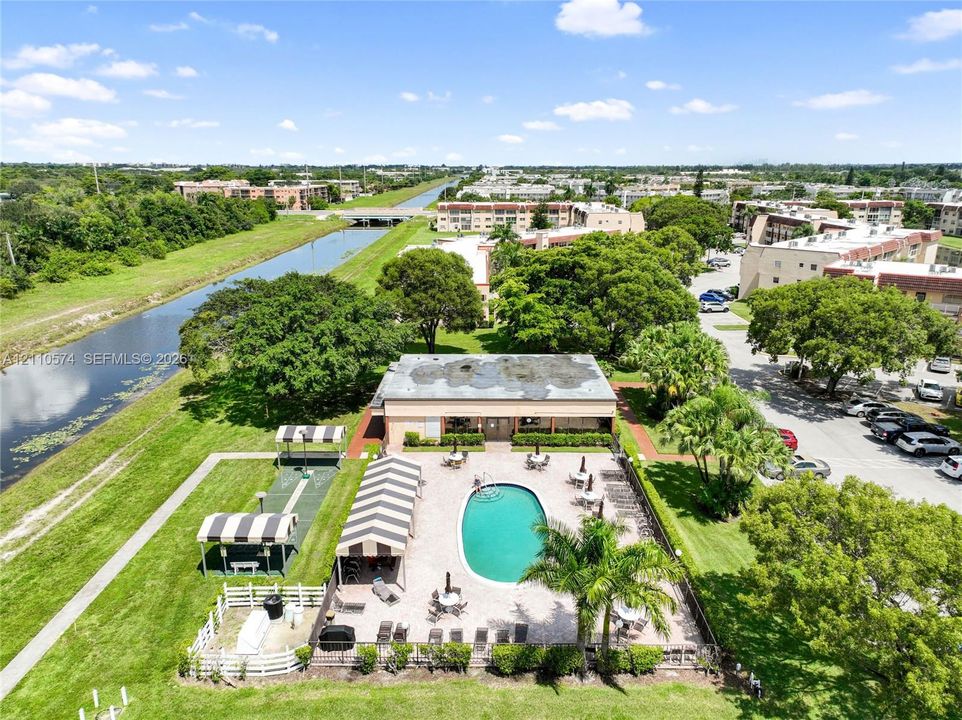 Outdoor swimming pool with paver patio, striped canvas awnings, adjacent lawn space, and proximity to canal frontage