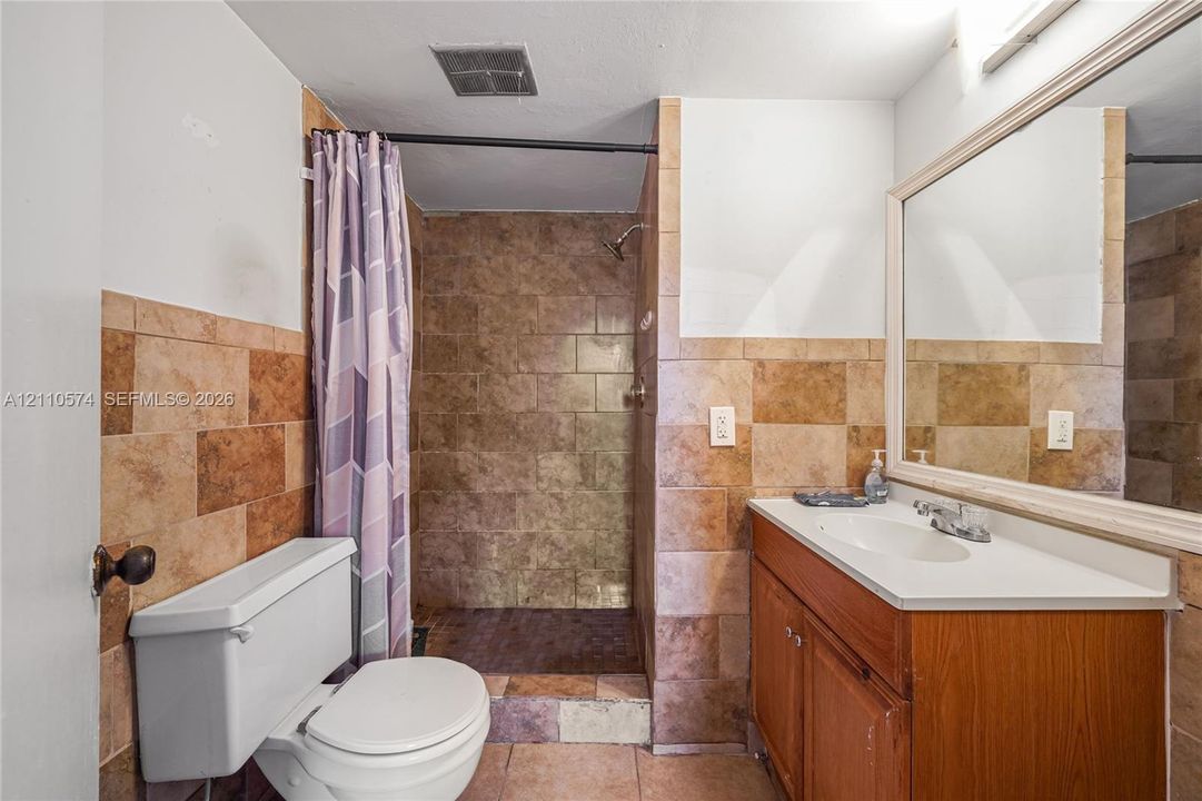 Bathroom featuring a wood-toned vanity with an integrated white basin, wall-mounted mirror with a wood-finish frame, and stone-tile wall accents extending through the walk-in shower area