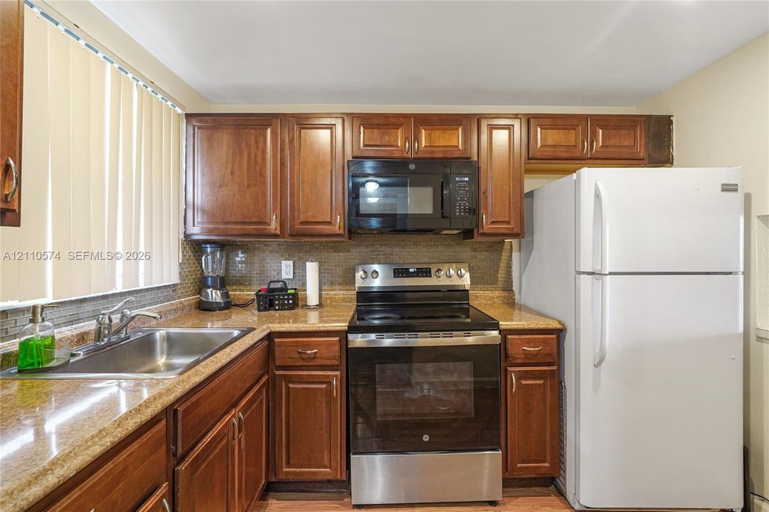 Kitchen featuring stained wood cabinetry, stone-finish countertops, tile backsplash, and stainless steel appliances